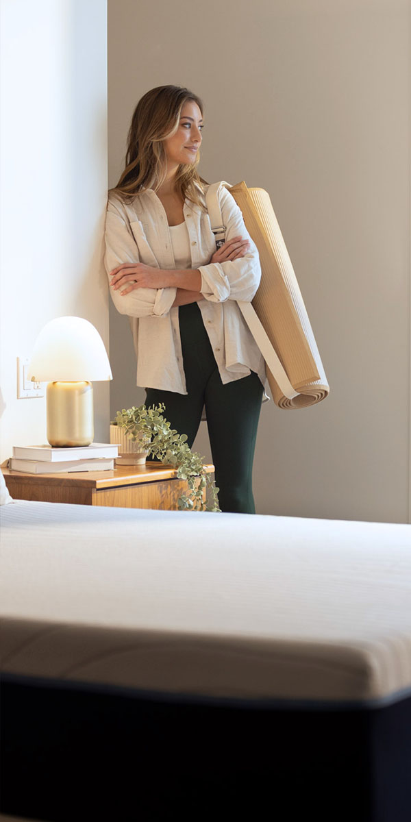 A confident woman holding a yoga mat standing in front of an Octave mattress